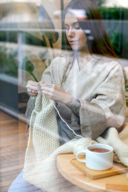 Donna del colpo medio che lavora a maglia all'interno