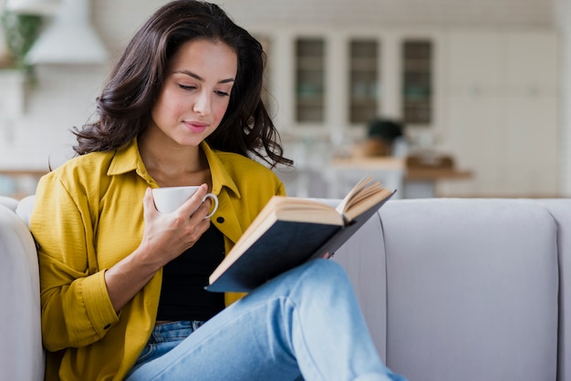 Donna del colpo medio con il libro e la tazza in salone