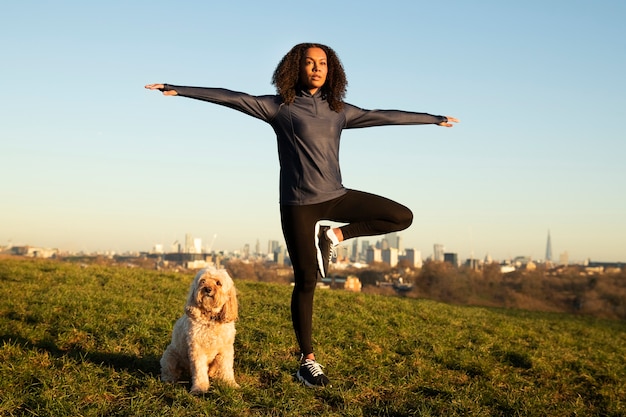 Donna del colpo pieno che fa yoga con il cane all'aperto