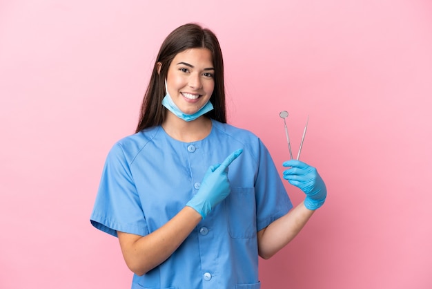 Donna del dentista che tiene gli strumenti isolati su sfondo rosa che punta al lato per presentare un prodotto