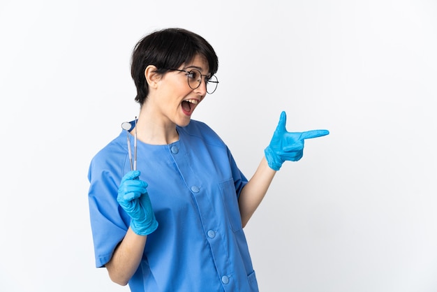 Donna del dentista che tiene gli strumenti isolati sulla parete rosa che indica il dito a lato e che presenta un prodotto