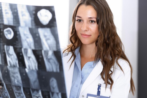 Donna del medico che esamina l'immagine a raggi X mentre si trova vicino alla finestra in ospedale. Chirurgo o ortopedico al lavoro. Concetto di medicina e assistenza sanitaria.