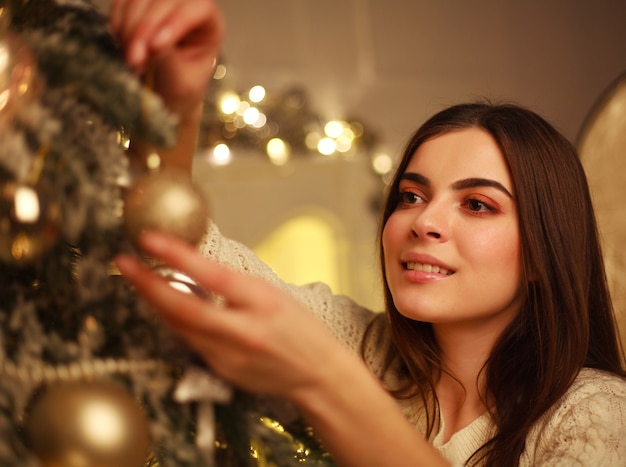 Donna del primo piano che decora i giocattoli del nuovo anno dell'albero di Natale a casa