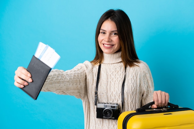 Donna del viaggiatore che tiene una valigia e un passaporto sopra la parete blu isolata