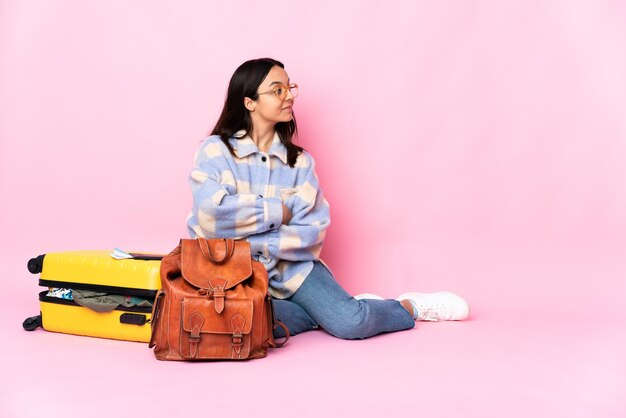 Donna del viaggiatore con una valigia che si siede sul pavimento in posizione laterale