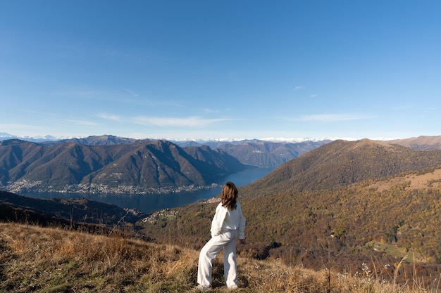 Donna del viaggiatore vestita di bianco sulla cima della montagna che ammira il paesaggio del lago di como italia