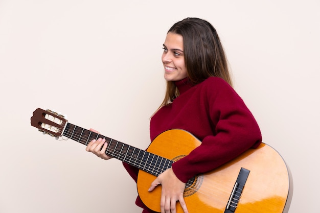 Donna dell'adolescente con la chitarra sopra la parete isolata che sembra laterale