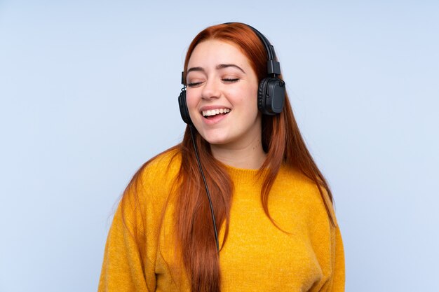 Donna dell'adolescente della testarossa sopra musica d'ascolto isolata della parete blu