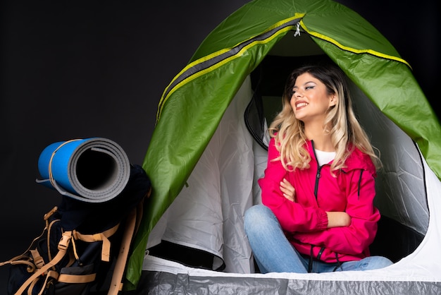 Donna dell'adolescente dentro una tenda verde di campeggio isolata sulla parete nera felice e sorridente