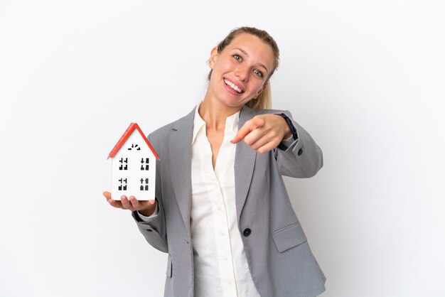 Donna dell'agente immobiliare che tiene una casa del giocattolo isolata su fondo bianco che indica davanti con l'espressione felice