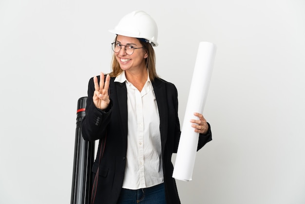 Donna dell'architetto di mezza età con il casco e che tiene le cianografie sopra fondo isolato felice e contando tre con le dita