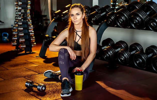 Donna dell'atleta di forma fisica che si siede in palestra accanto a una bottiglia di acqua