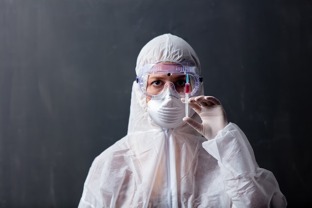 Donna dell'erba medica che indossa indumenti protettivi contro il virus con la siringa