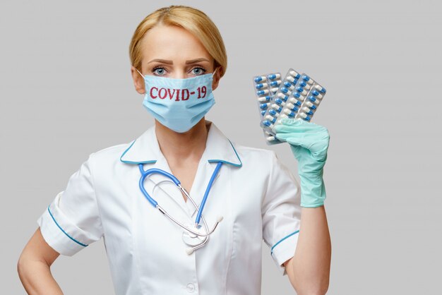 Donna dell'infermiere del medico che indossa i guanti protettivi del lattice e della maschera che tengono le bolle delle pillole