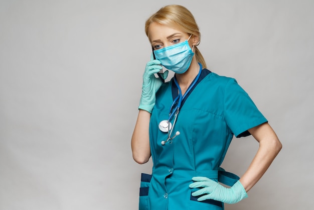 Donna dell'infermiere del medico che indossa i guanti protettivi del lattice e della maschera - parlando al telefono