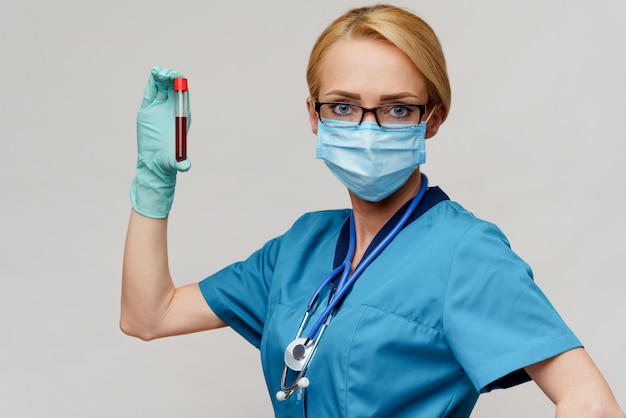 Donna dell'infermiere di medico che indossa maschera protettiva e guanti - tenendo la provetta dell'analisi del sangue del virus