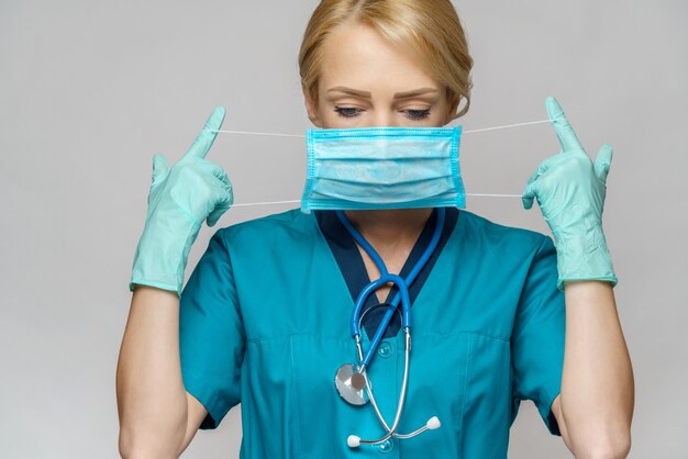 Donna dell'infermiere di medico con lo stetoscopio sopra la parete grigio chiaro - mostrando maschera protettiva