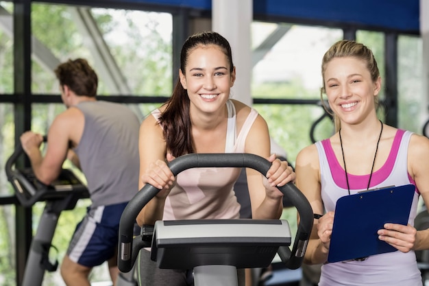 Donna dell&#39;istruttore che parla con una donna che fa la bici di esercizio alla palestra