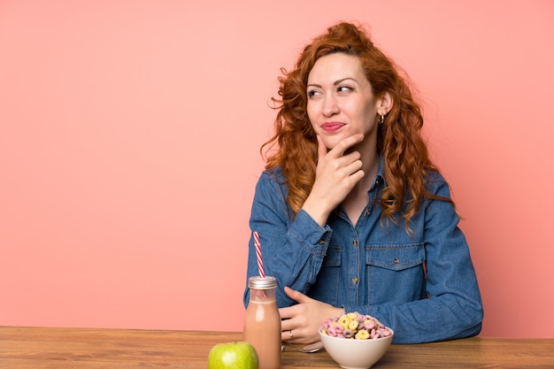 Donna della testarossa che mangia i cereali e la frutta di prima colazione che pensano un'idea