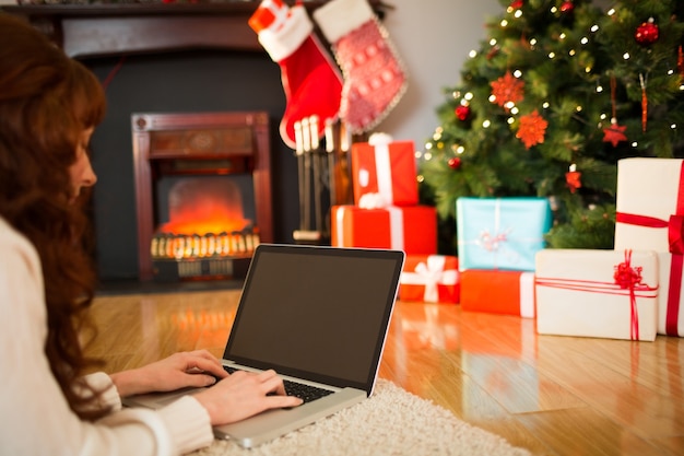 Donna della testarossa che si trova sul pavimento facendo uso del computer portatile a natale