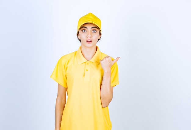 Donna delle consegne in uniforme gialla in piedi e che mostra due dita vicino agli occhi.