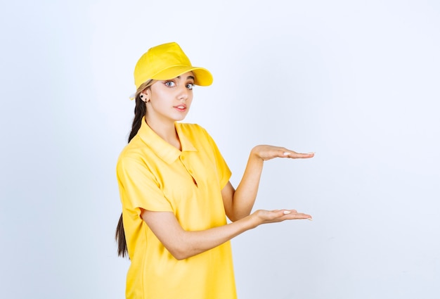 Donna delle consegne in uniforme gialla in piedi e che mostra le dimensioni con le mani.