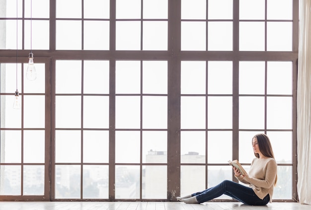 Donna delle tenaglie che si siede sul pavimento vicino al libro di lettura della finestra