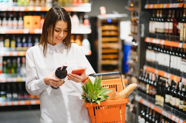 Donna dello shopping guardando gli scaffali del supermercato. Ritratto di una giovane ragazza in un negozio di mercato con carrello nel settore dell'alcol.