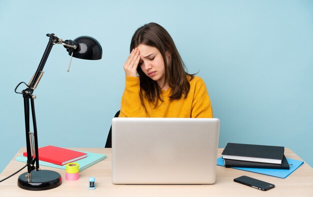 Donna dello studente che studia nella sua casa isolata sulla parete blu con l'emicrania