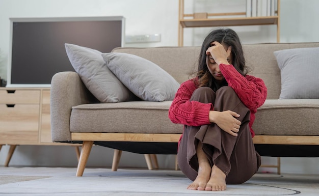 Donna depressa sola e infelice mentale seduta da sola sul divano a casa con la mano sul viso sentirsi stress triste e preoccupata delusione mentre affronta problemi durante la pandemia di coronavirus o covid19