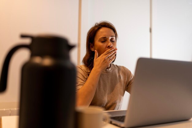 Donna di 40 anni che sbadiglia stanca a casa o in ufficio con il computer portatile che lavora tardi in ufficio