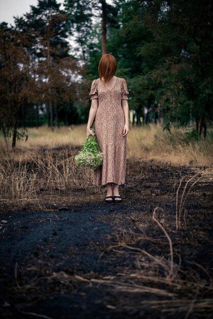 Donna di 40 anni con un mazzo di fiori di campo sulla terra bruciata, concetto di burnout psicologico