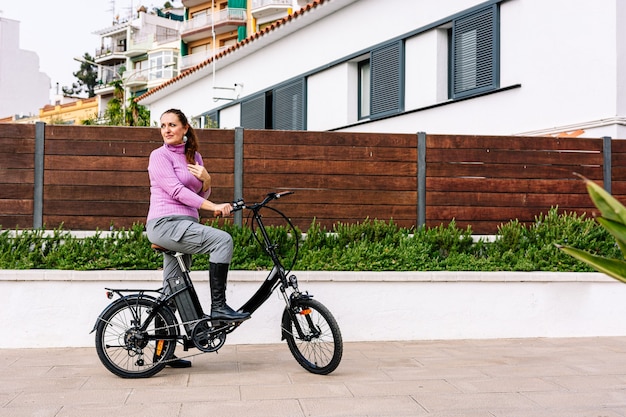 Donna di 40 anni in sella alla sua bicicletta elettrica per le strade della città (Concetto di mobilità elettrica)