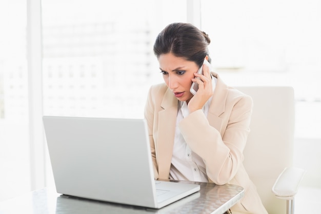 Donna di affari accigliata che lavora con un computer portatile sul telefono