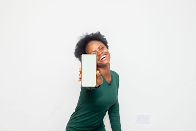 Donna di affari africana emozionante che mostra il telefono cellulare in bianco dello schermo isolato sopra priorità bassa bianca