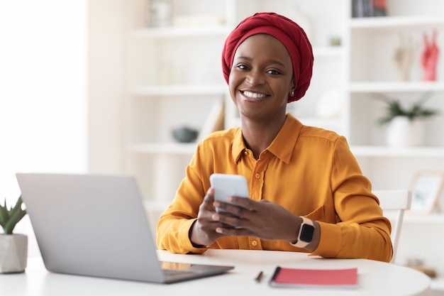 Donna di affari afroamericana allegra che utilizza smartphone e laptop