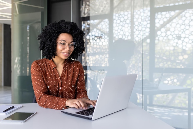 Donna di affari afroamericana felice e sorridente che digita sull'impiegato del computer portatile con capelli ricci e