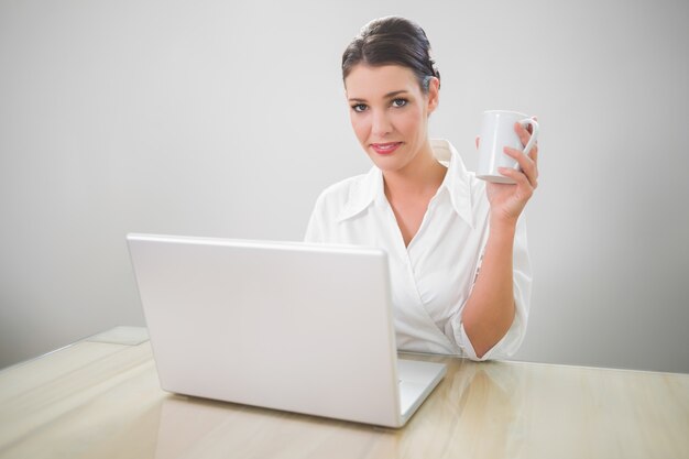 Donna di affari allegra che lavora al caffè della tenuta del computer portatile