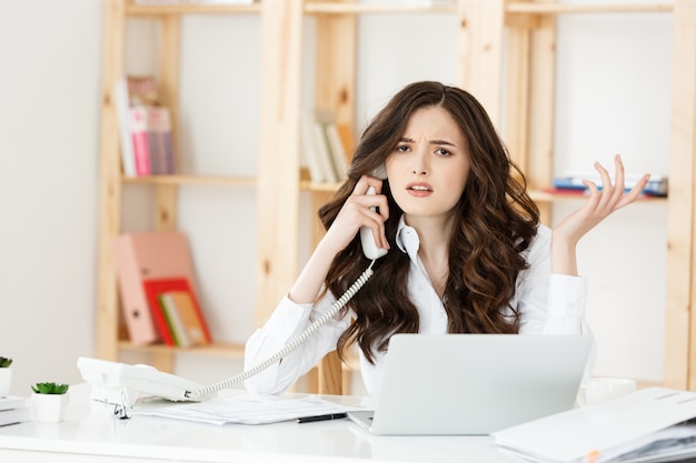 Donna di affari arrabbiata che grida sul telefono in ufficio moderno