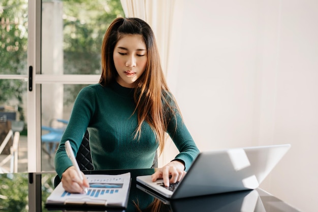 Donna di affari asiatica che lavora nell'ufficio con i documenti del computer portatile e della compressa del blocco note xA