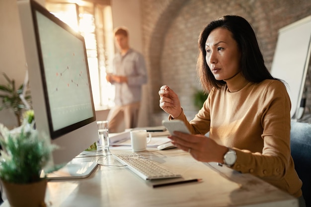 Donna di affari asiatica che legge i rapporti su un computer mentre woeking in ufficio