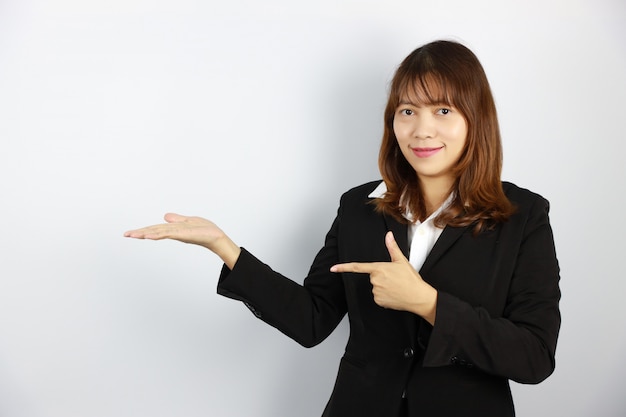 Donna di affari asiatica che mostra qualcosa con il fronte sorridente e sicuro su bianco