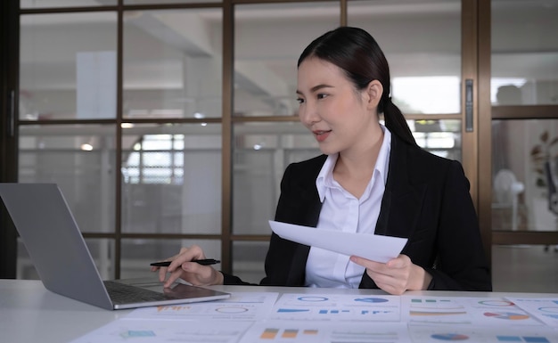 Donna di affari asiatica che si siede sul lavoro su un computer portatile in ufficio