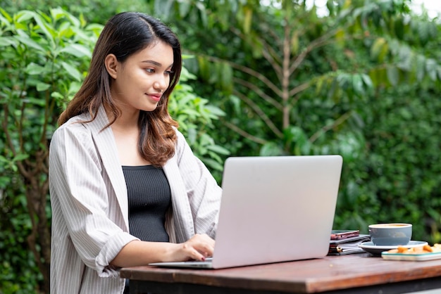 Donna di affari asiatica che utilizza un computer portatile con un taccuino del telefono cellulare e una tazza di caffè sulla tavola