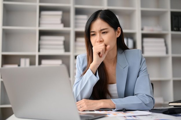 Donna di affari asiatica premurosa che esamina il suo pensiero pensieroso dello schermo del computer portatile