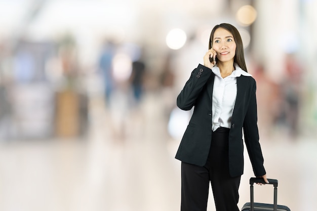 Donna di affari asiatica sorridente che cammina con il suo bagaglio in aeroporto