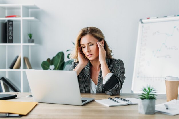 Donna di affari attraente che ha mal di testa e guardando il computer portatile in ufficio