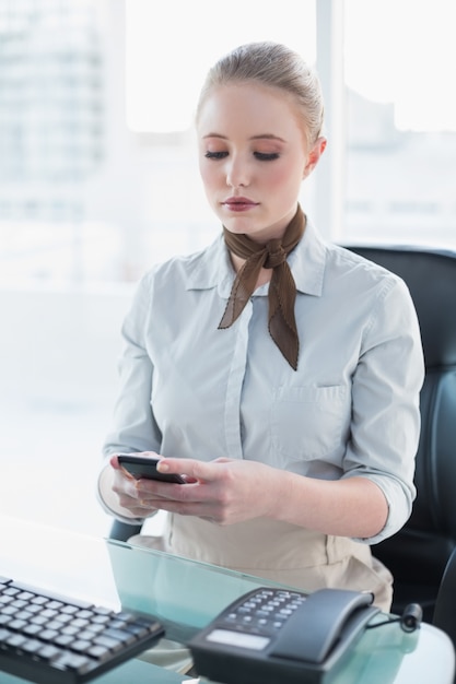 Donna di affari bionda severa che per mezzo dello smartphone