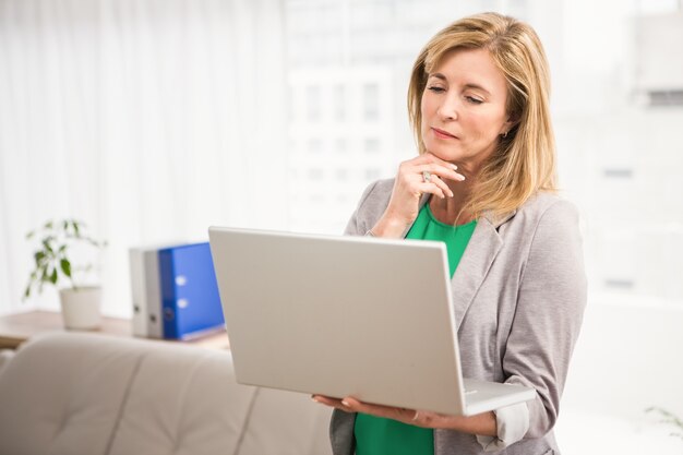 Donna di affari casuale concentrata che lavora con il computer portatile