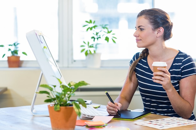 Donna di affari casuale sorridente che lavora al digitalizzatore e che tiene caffè